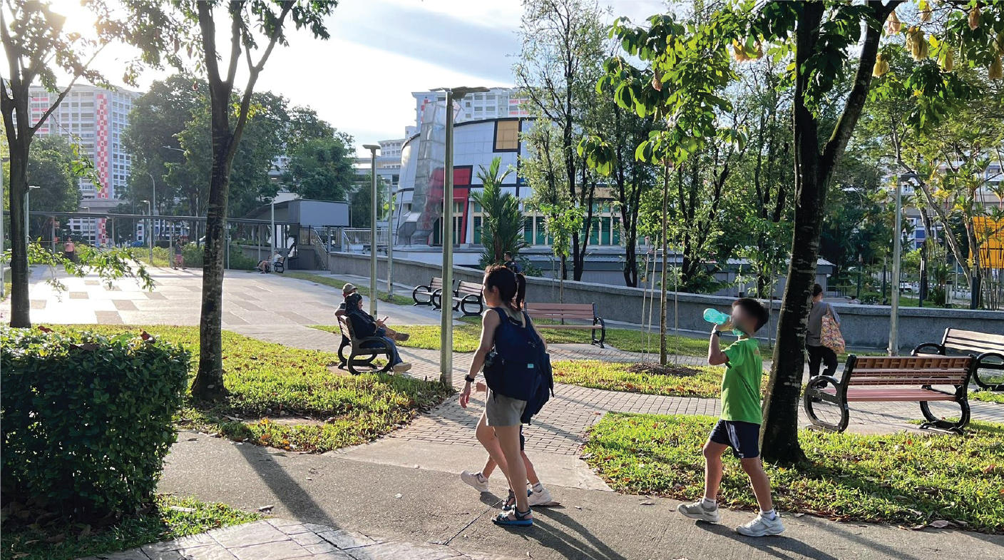 People enjoying a sunny day in a park with benches, trees, and buildings in the background.